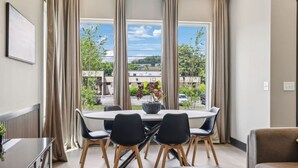 A modern dining area with a round table, black chairs, and a view of a cityscape through large windows.