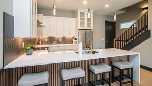 A modern kitchen with a central island, bar stools, pendant lighting, and a staircase. - East Nash Luxury Escape w/Rooftop Deck-Sleeps 12! (Nashville)