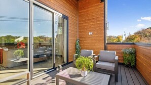 A wooden deck with a glass door leading to a balcony, furnished with a table, chairs, and potted plants. - East Nash Luxury Escape w/Rooftop Deck-Sleeps 12! (Nashville)