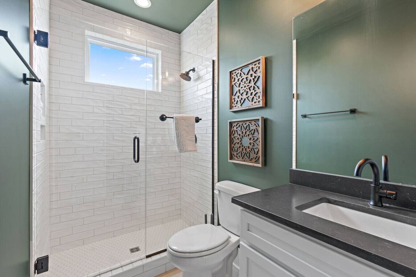 Un baño con ducha envuelta en vidrio, inodoro, lavamanos con espejo y paneles decorativos en la pared.
