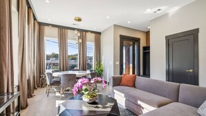 Een moderne woonkamer met een grijze bank, een bijzettafel met een plant, en een eethoek met een stoel en tafel.