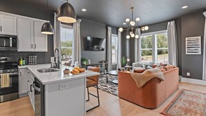 Cozinha moderna com armários brancos, uma ilha central e um espaço de refeições com sofá marrom.