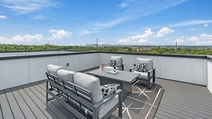 Terraço no telhado com deck de madeira, um sofá, duas poltronas e uma mesa pequena.