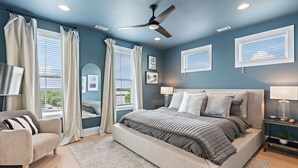 Quarto com uma cama grande, um ventilador de teto e vista para o exterior pelas janelas.