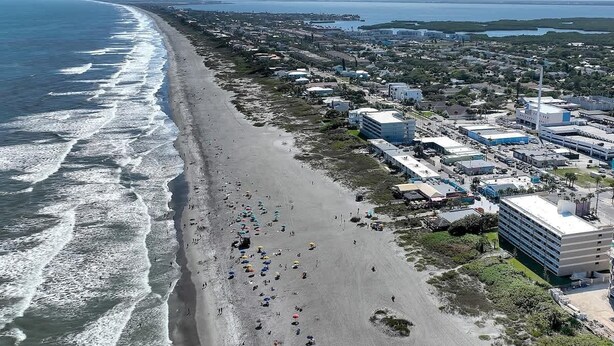 Vista aérea de una zona costera con playa, edificios y cielo despejado.