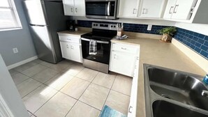 Una cocina moderna con armarios blancos, un refrigerador de acero inoxidable, un microondas, un horno y un fregadero.