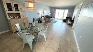 Un amplio espacio de sala con una mesa de vidrio, sillas blancas, un sofá y un ventanal grande.