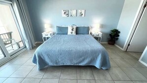 Un dormitorio con una cama grande, dos mesitas de noche, una ventana con cortinas y una planta en maceta.