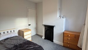Un dormitorio con cama, cómoda, mesita de noche, chimenea y lámpara en el techo.