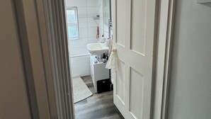 Pasillo que conduce a un baño con lavamanos, espejo y perchero.