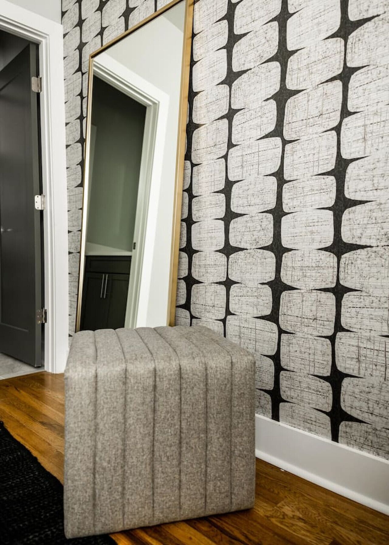 Une pièce avec un banc recouvert d’un tissu gris, un papier peint à motifs et un plancher en bois.
