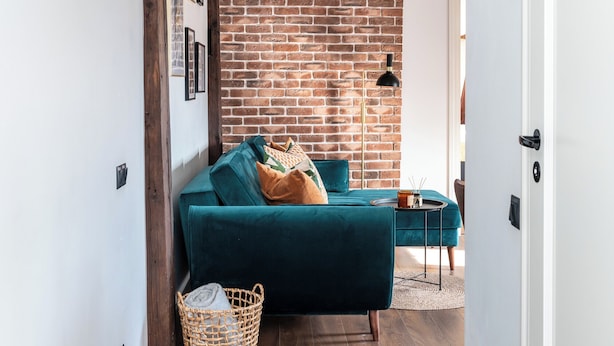 A hallway with a brick wall, wooden beams, a teal sofa, and a wicker basket. - Toompea Castle 2-Storey Unique Apartment (Tallinn)