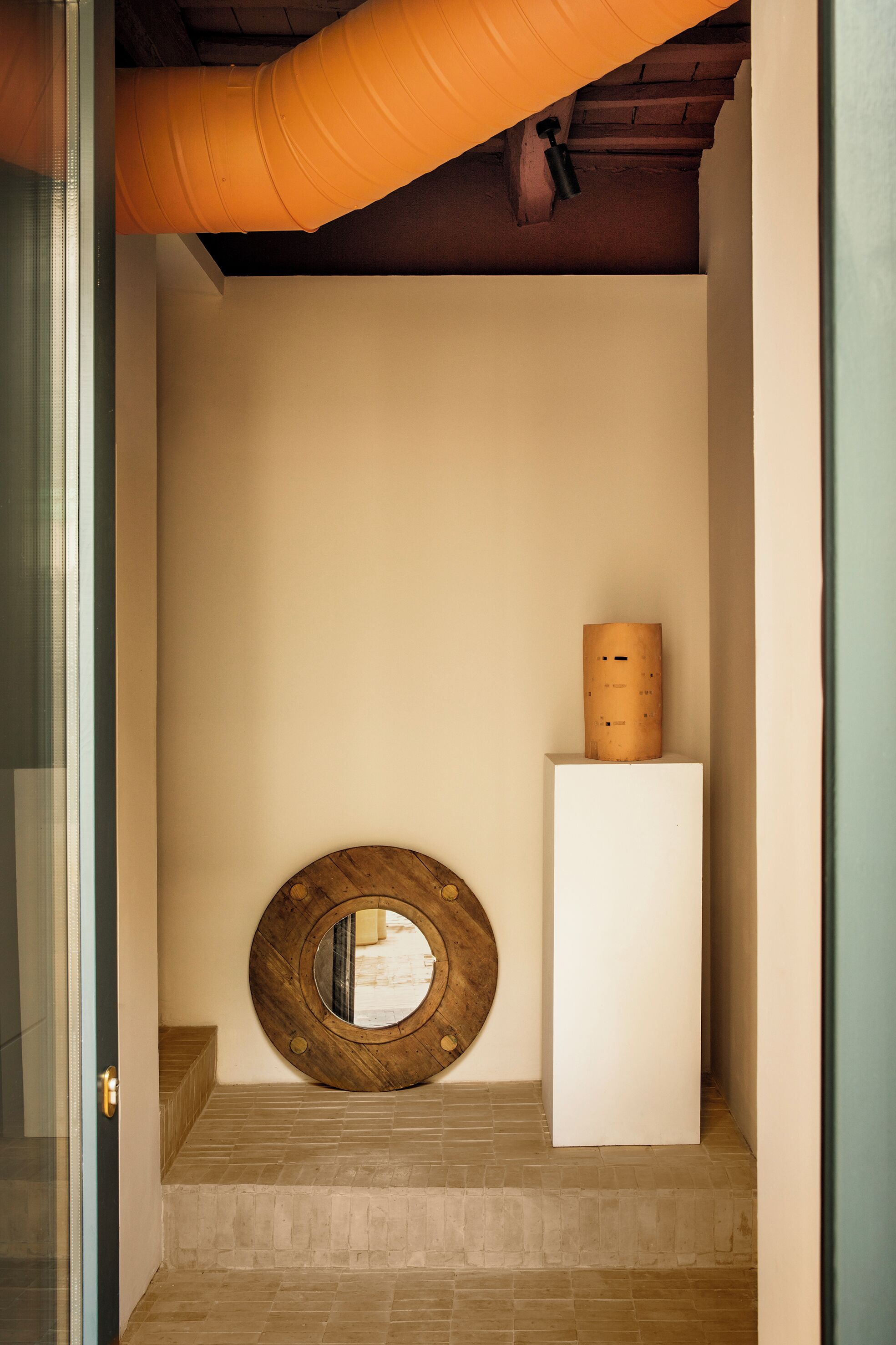 Een gang met een ronde spiegel van hout, een witte zuil en een structuurwand.