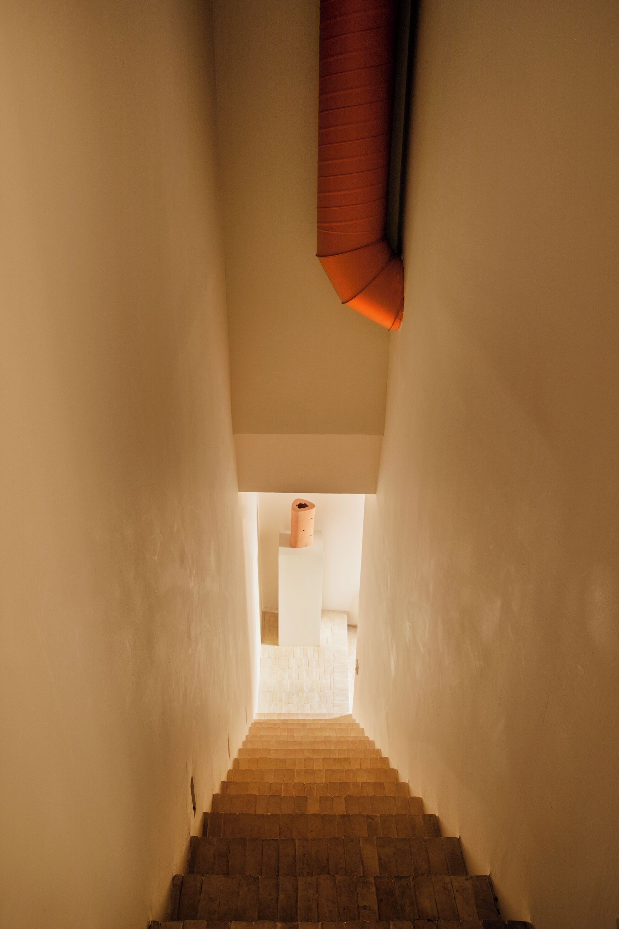 Una escalera estrecha con barandal de madera y una lámpara colgante.