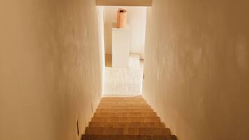 Una escalera estrecha con barandal de madera y una lámpara colgante.