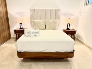 Una cama con estructura de madera, dos mesitas de noche con lámparas y un cabecero.