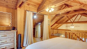 Camera da letto in una baita di legno, con un letto, una cassettiera e una ventola a soffitto.