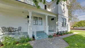 Une maison à deux étages dotée d’un porche abrité, d’un escalier menant à l’entrée et d’un petit espace extérieur aménagé avec des chaises.