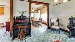 Une pièce avec un piano, une table à manger entourée de chaises, un tapis à motifs et un lustre.