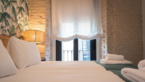 A hotel room with a large bed, a window with curtains, a lamp, and a view of the outside.