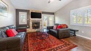 A living room with a fireplace, leather sofas, a glass coffee table, and a ceiling fan. - 4 mi to Aggieland, Yard & Deck (Bryan)