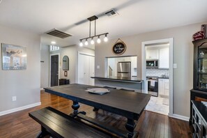 A modern kitchen with a central island, stainless steel appliances, and a dining area with a bench. - 4 mi to Aggieland, Yard & Deck (Bryan)