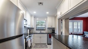 A modern kitchen with white cabinets, a stainless steel refrigerator, a built-in oven, and a black granite countertop. - 4 mi to Aggieland, Yard & Deck (Bryan)