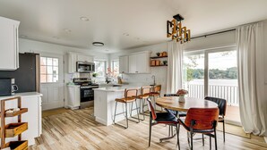 A modern kitchen with white cabinetry, a central island, and a dining area with wooden chairs. - Direct Lakefront Retreat | Indian Ranch | Casinos (Thompson)