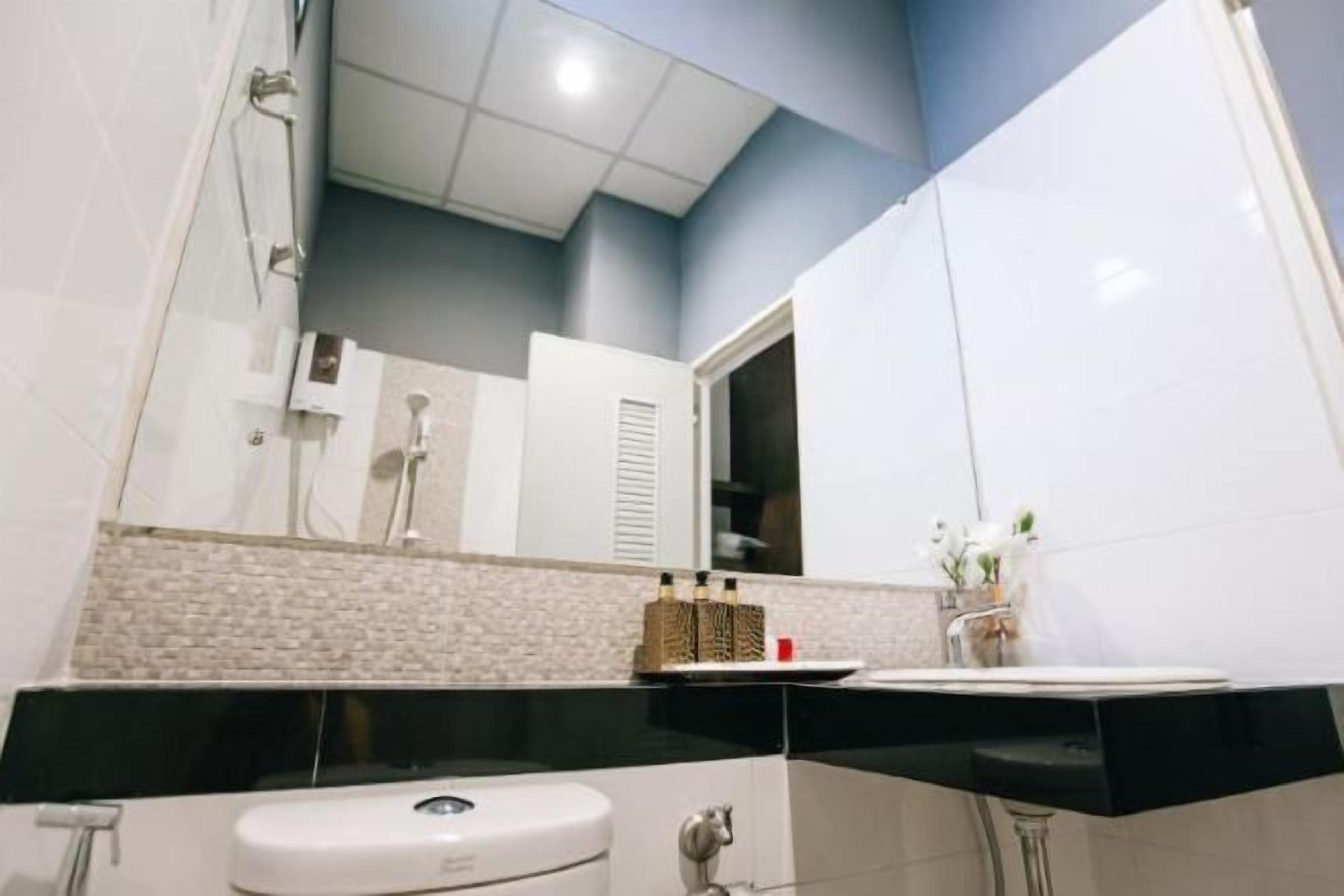 A modern bathroom with a black countertop, white sink, and a mirror above the sink. There is a shower area visible in the background.