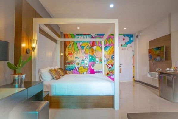 A modern hotel room with a bed, a small desk, a potted plant, and a colorful mural on the wall.