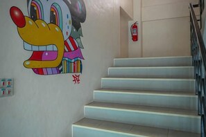 Un escalier orné d’une fresque murale colorée, un extincteur et une main courante.