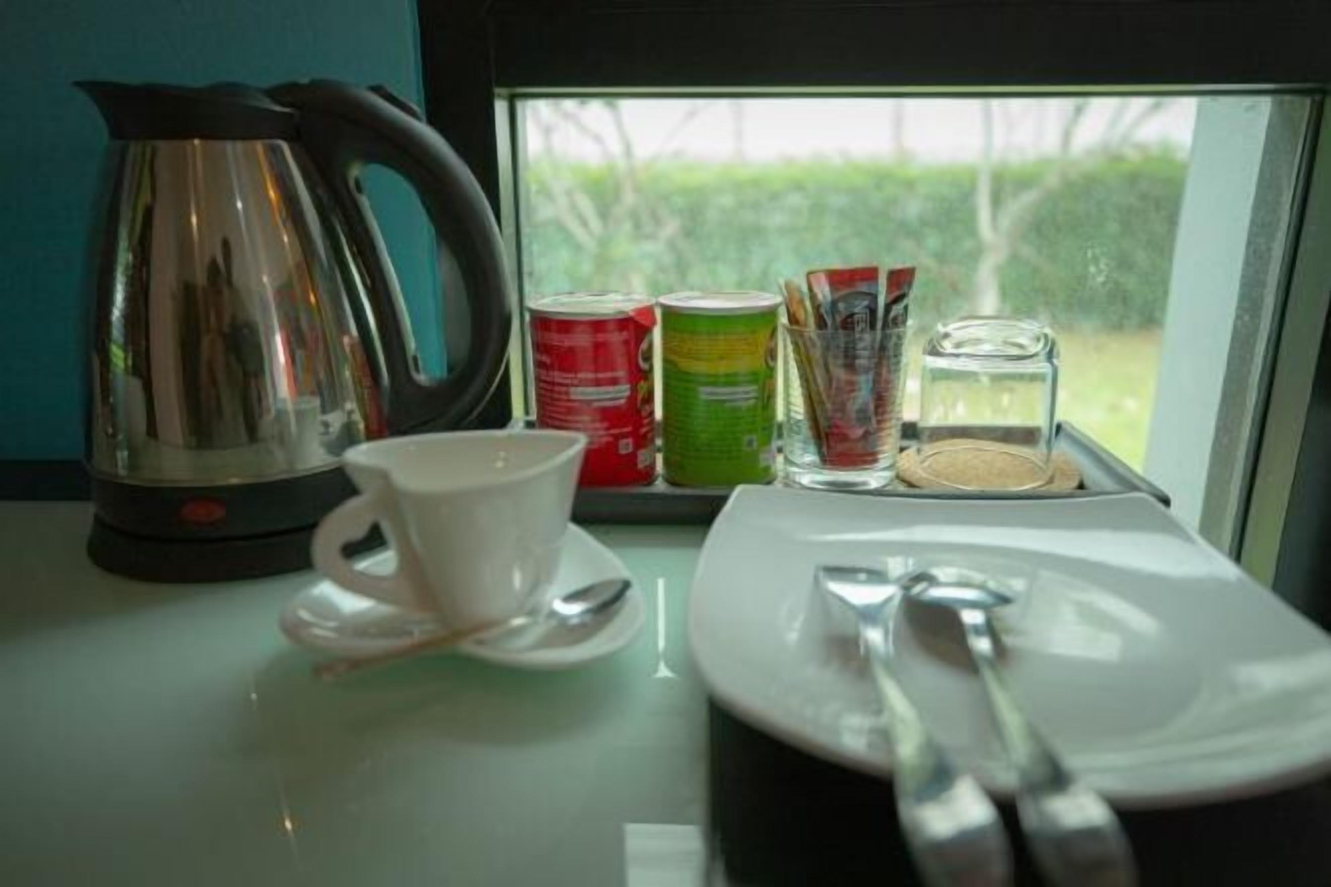 Ein Tisch mit einem Wasserkocher, einer Tasse, einem Untertasse, einem Teller mit Besteck und Speisen.