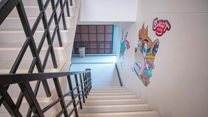 A staircase with a metal railing, a wall with a cartoon character, and a window in the background. - Smart Hotel (Lam Luk Ka)