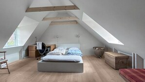 Een slaapkamer in loftstijl met een schuine kap, een bed, een bureau en een stoel.