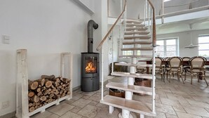 Een modern interieur met een houtkachel, een rustieke trap en een eetgedeelte met stoelen.