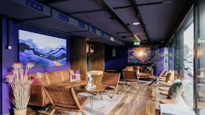 Ein modernes Interieur mit einer Couch, Sesseln und einem Tisch. Große Fenster und Kunstwerke schmücken die Wände.