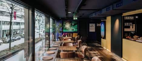 A restaurant with long tables and chairs, a view of the street outside, and a menu display on the right.