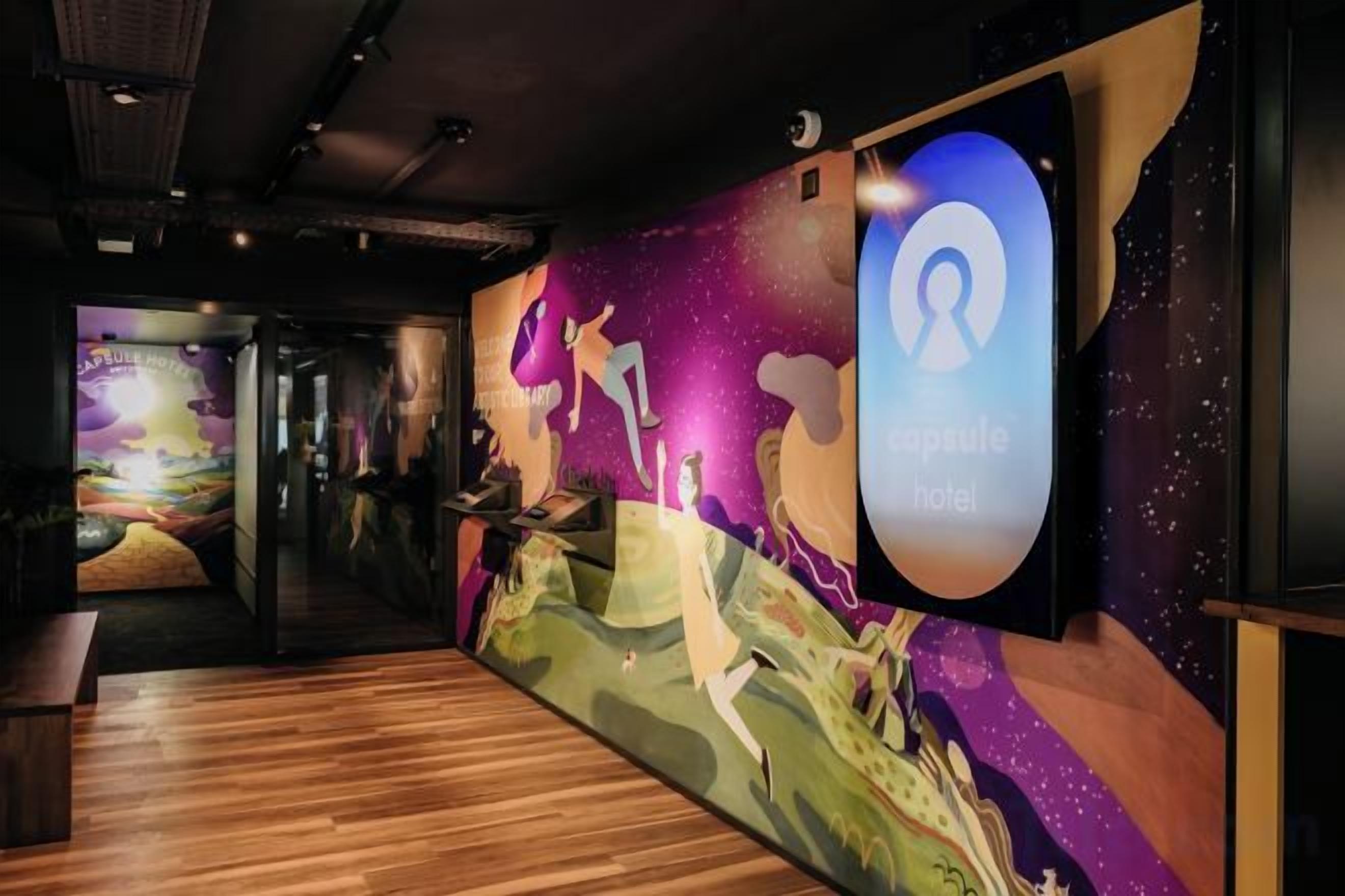 A hotel corridor with a mural, a reception area, and a digital guest ID display.