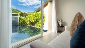 Una camera moderna con un balcone in vetro che si affaccia su un giardino e una piscina.