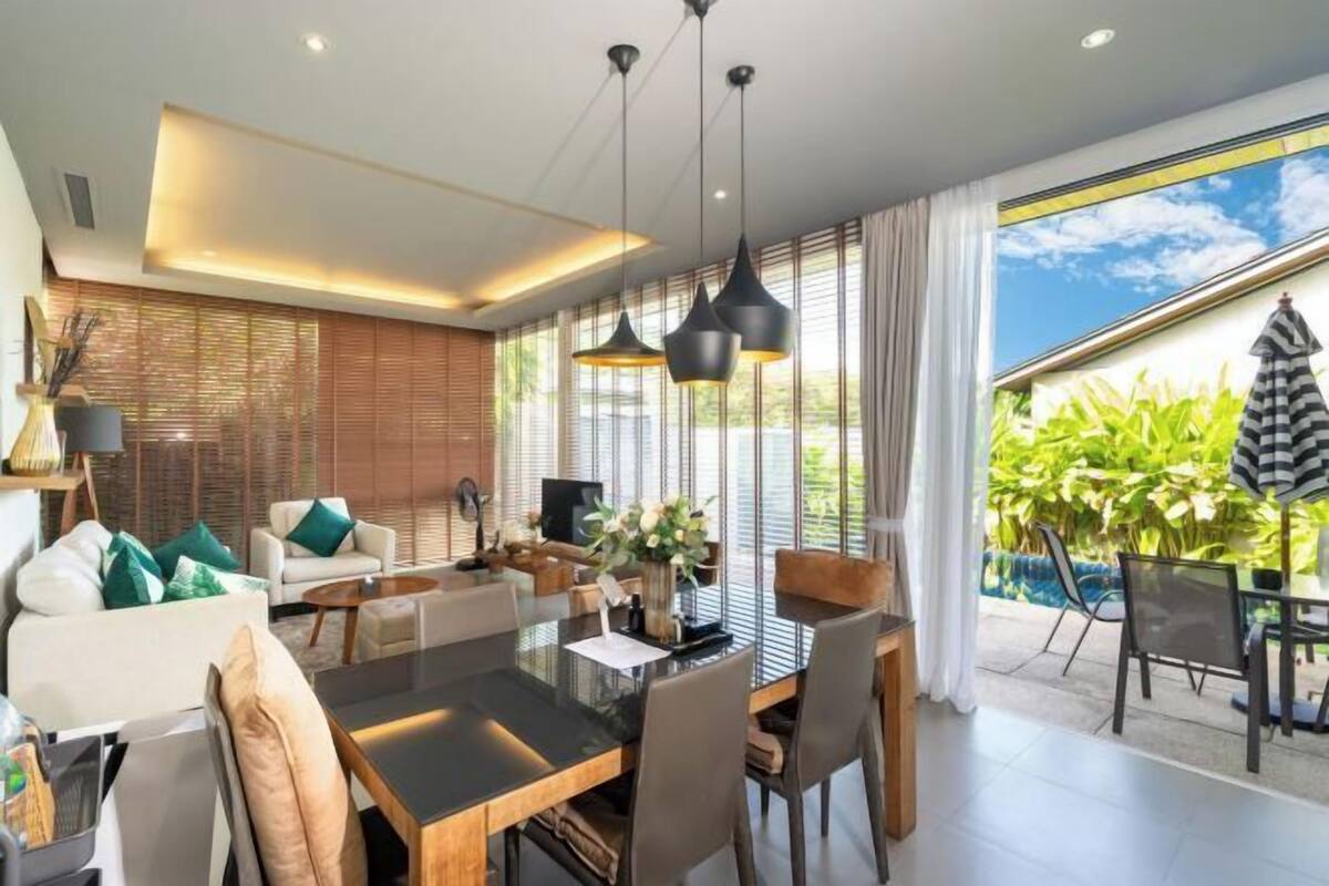 Een moderne woonkamer met een eethoek, grote ramen en uitzicht op groen.