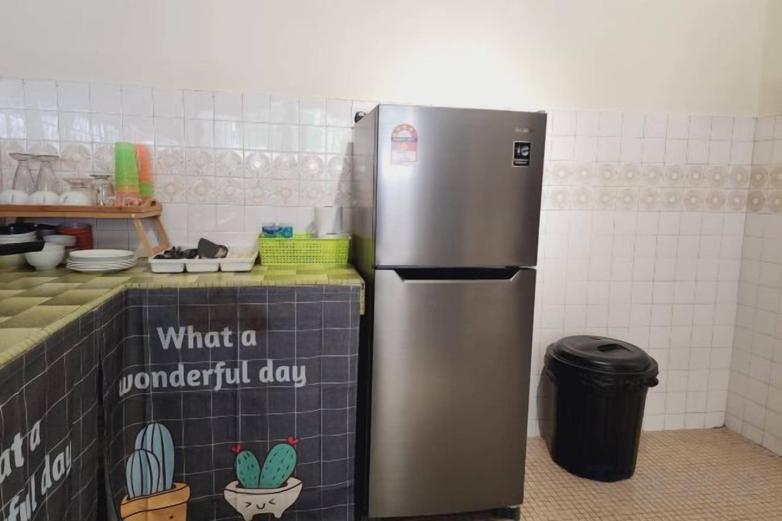 A kitchen with a stainless steel refrigerator, a trash bin, and a tiled backsplash.