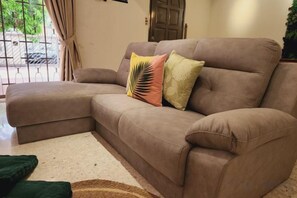 A brown sectional sofa with two decorative pillows, a woven rug, and a door in the background. - Damansara Jaya Petaling Jaya 2 Storey Landed House for 15 Pax (Petaling Jaya)
