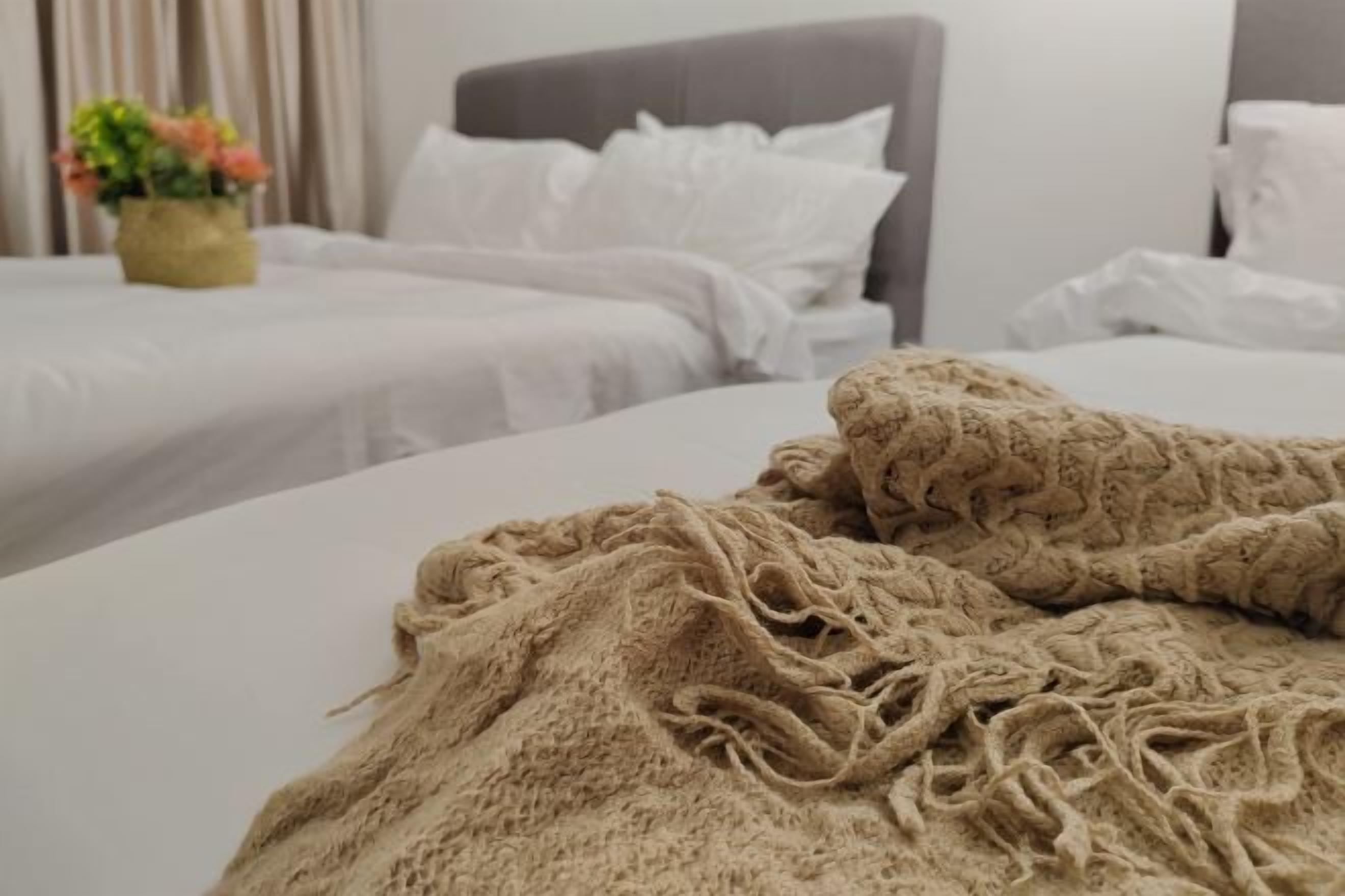 A hotel room with a bed covered in a textured beige blanket, a grey headboard, and white bedding.