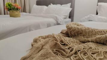 A hotel room with a bed covered in a textured beige blanket, a grey headboard, and white bedding.