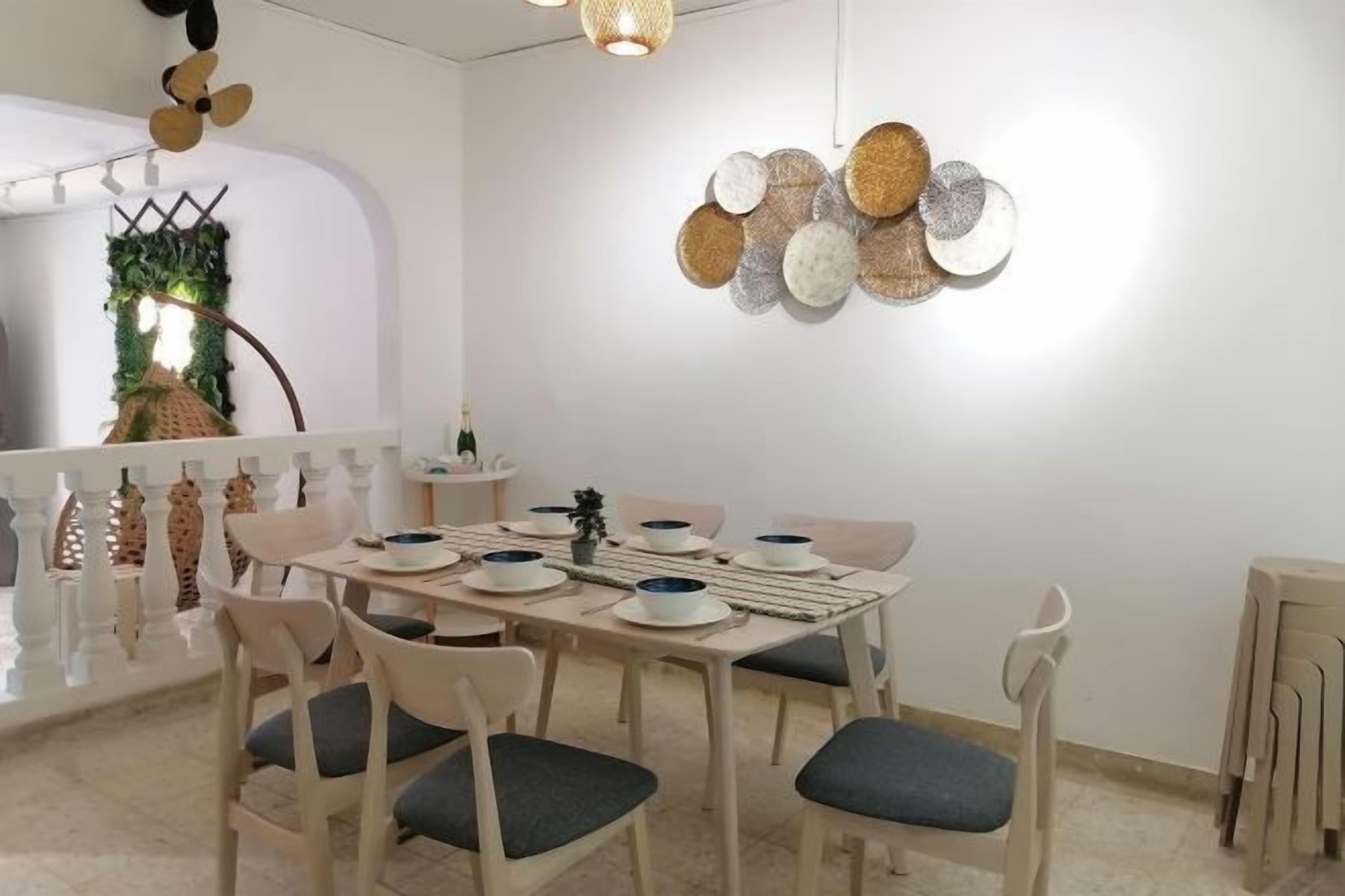A dining area with a round table set for six, surrounded by six chairs with cushions.