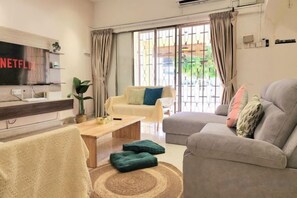A living room with a flat-screen TV, a sofa, a coffee table, and a window with curtains. - Damansara Jaya Petaling Jaya 2 Storey Landed House for 15 Pax (Petaling Jaya)