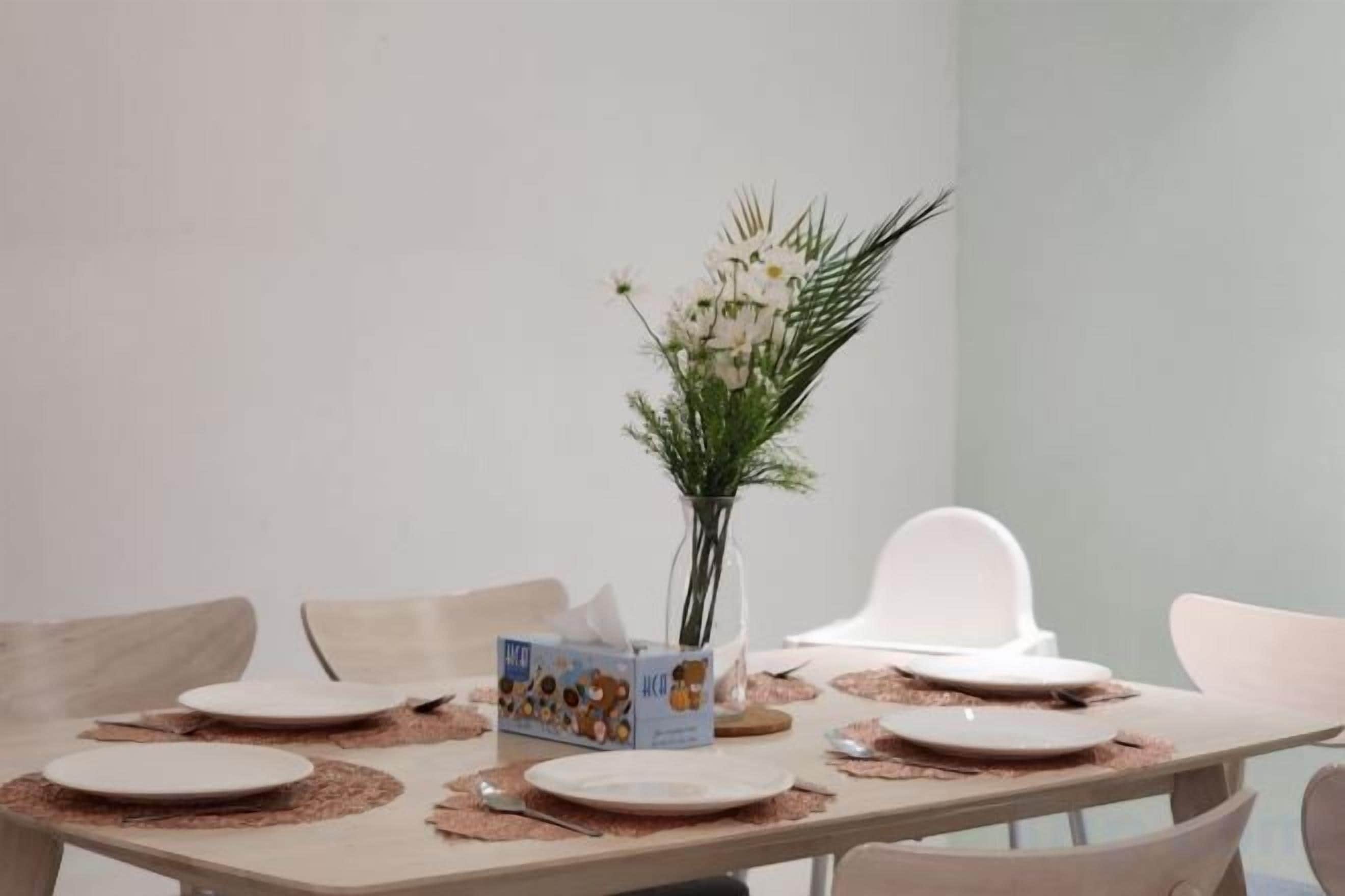 A dining table set with placemats, plates, a vase with flowers, and a box of cereal.