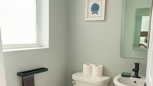 Un baño con inodoro, lavamanos y una obra de arte con una concha enmarcada en la pared.