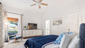Une chambre à coucher avec un lit, une commode, une chaise, un téléviseur et un ventilateur de plafond.