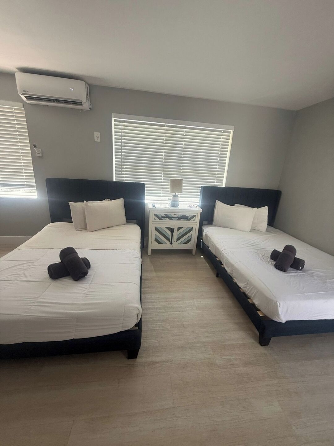 A room with two beds, a bedside table with a lamp, and an air conditioning unit.